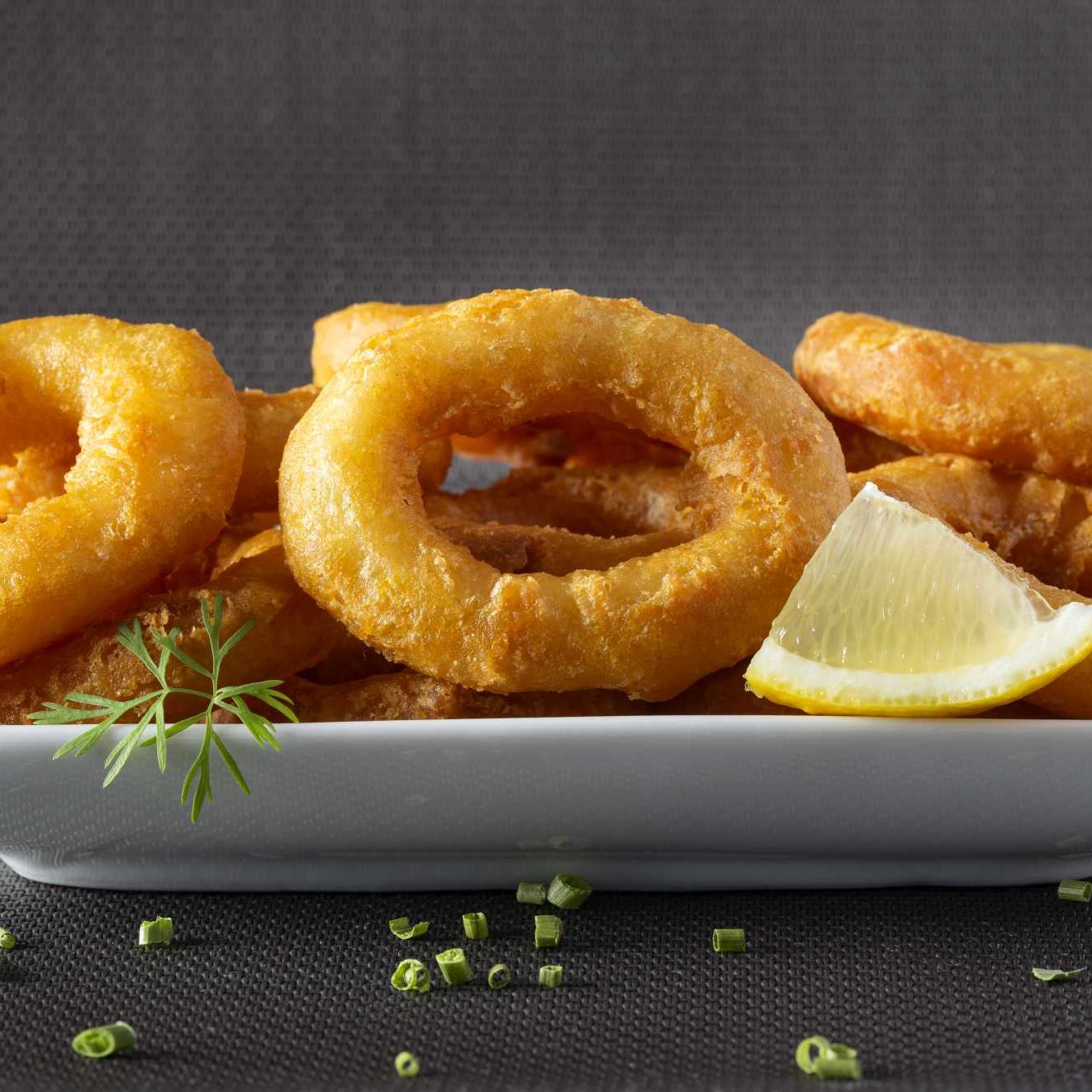 Fried calamari rings on plate with lemon and herbs