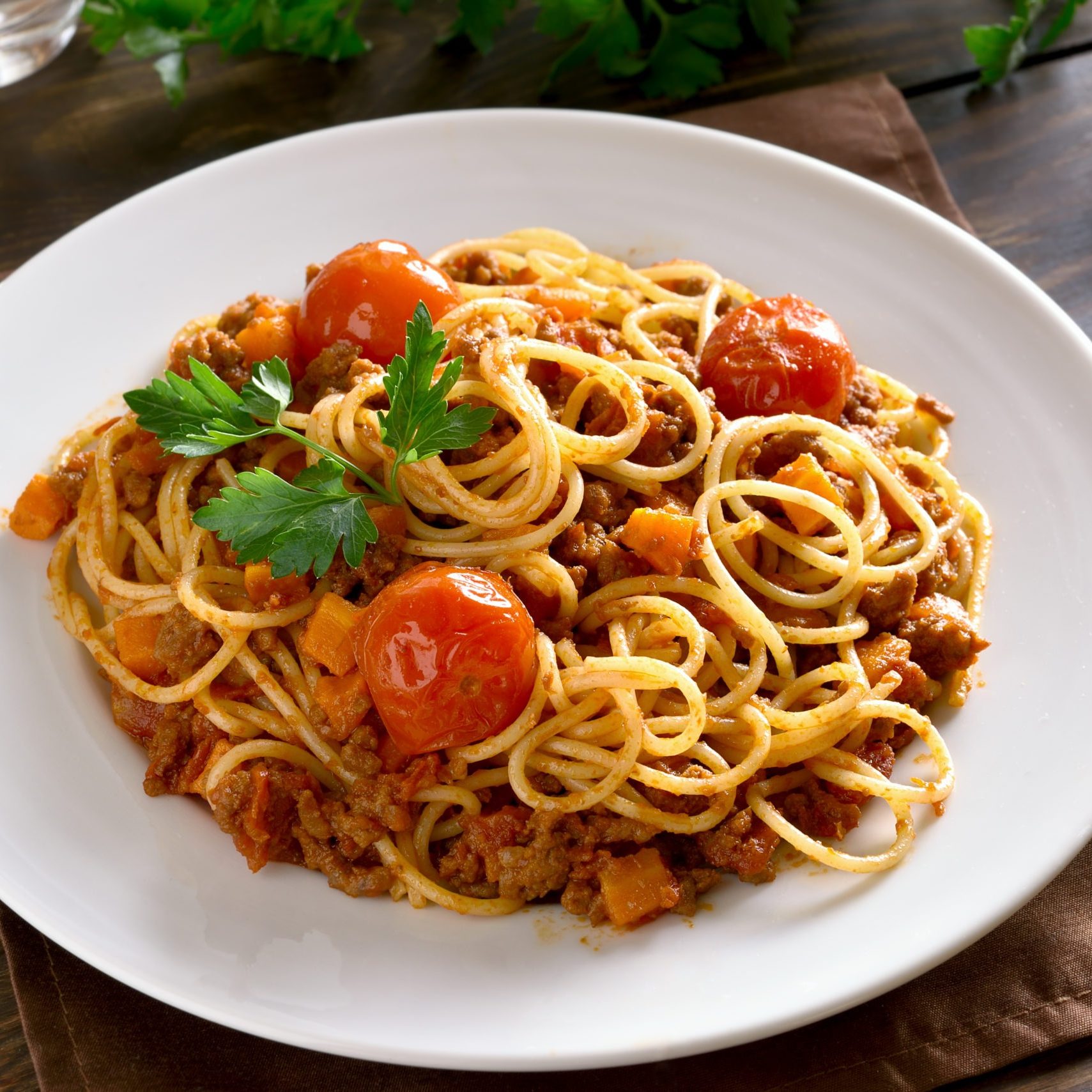 Close up of spaghetti with minced meat and vegetables on wooden table